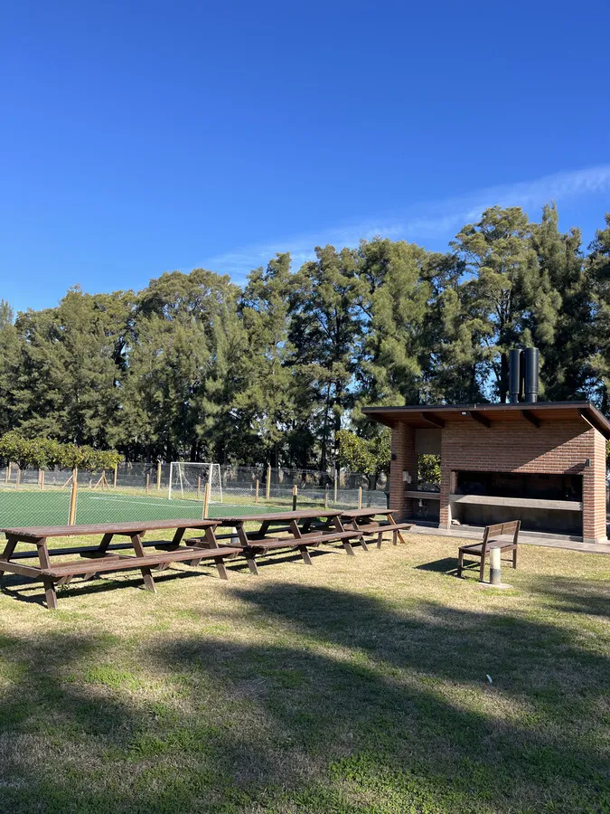 Quincho de madera con mesas largas junto a las canchas